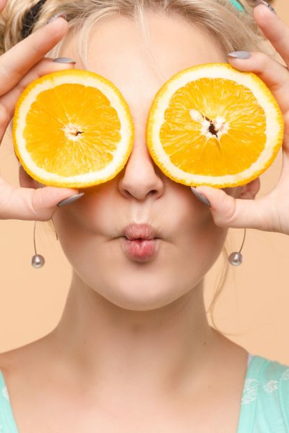 woman with a cool hairstyle holds 2 orange slices in her hands